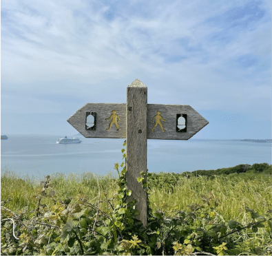 Wood sign with two options of directions with both the same symbol on it, on a grass verge with the sea in the background