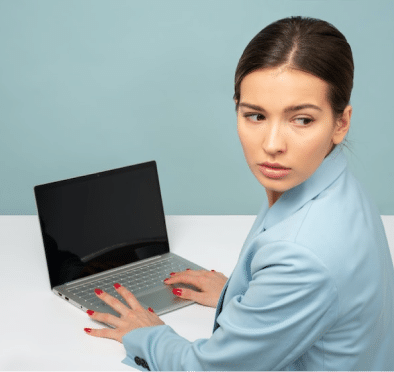 Women in a light blue suit, typing on a laptop whilst looking behind her back